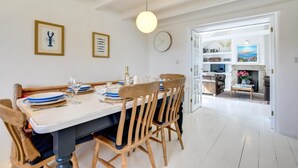 A dining area with a white table and wooden chairs, a clock on the wall, and framed artwork. - 3 Bed in Sennen (oc-thbyre) (Sennen)