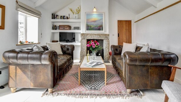 A living room with two leather sofas, a coffee table, a fireplace, and a bookshelf. - 3 Bed in Sennen (oc-thbyre) (Sennen)
