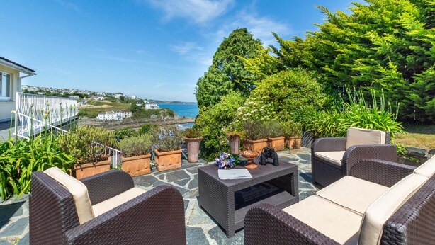 A patio with wicker furniture, potted plants, and a view of the sea and houses in the distance. - 3 Bed in Mevagissey (oc-windru) (Mevagissey)