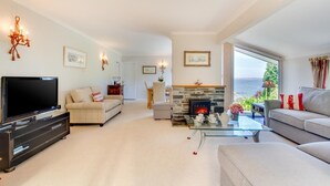 A spacious living room with a television, sofas, a fireplace, and a view of the sea. - 3 Bed in Mevagissey (oc-windru) (Mevagissey)