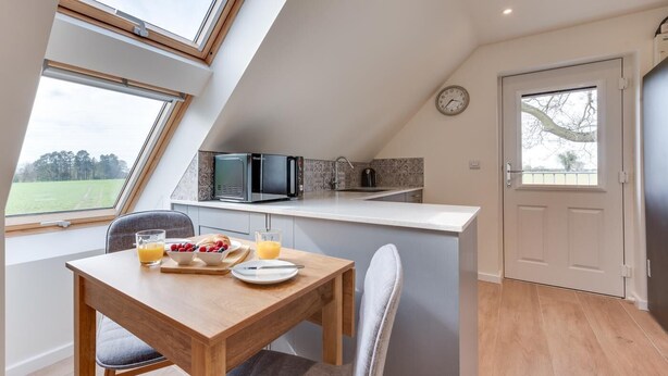 A modern kitchen with a built-in microwave, a small island with a sink, and a dining area with a table set for breakfast. - 1 Bed in Booton (oc-2266) (Cawston)