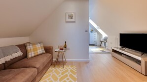 A modern living room with a sofa, a small table with a bottle and glasses, a TV, and a staircase leading to an upper level. - 1 Bed in Booton (oc-2266) (Cawston)