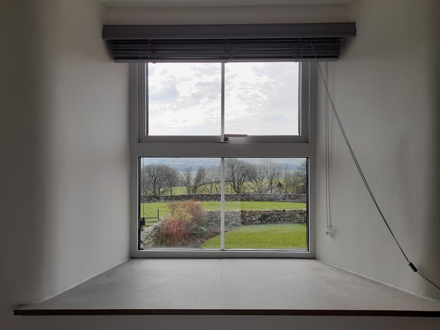Een kamer met een groot raam dat uitzicht biedt op een landelijk landschap, met velden en stenen muren.
