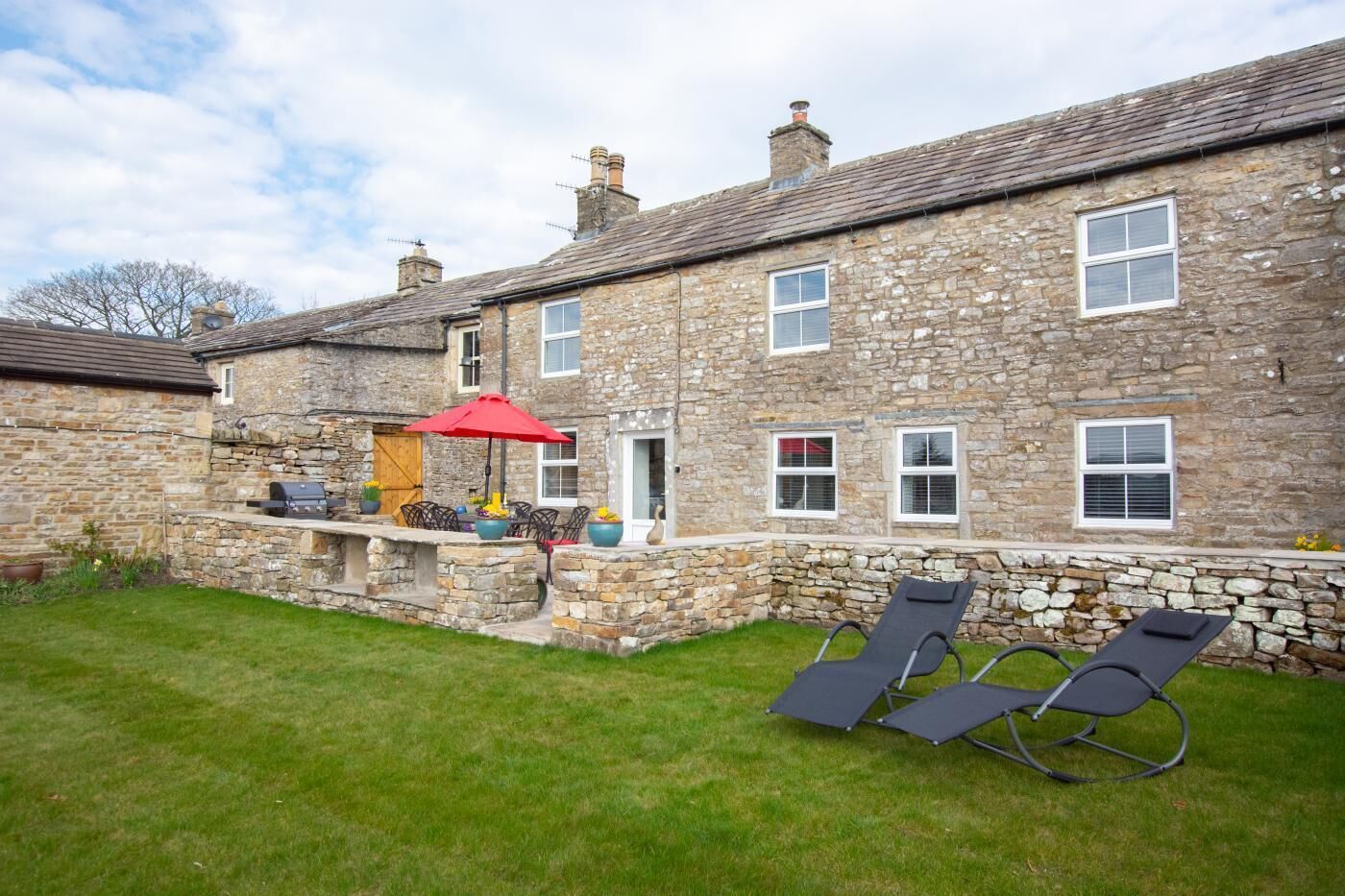 A stone house with a patio area, outdoor seating, and a lawn.