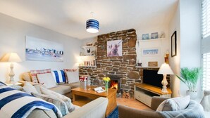 A cozy living room with a stone fireplace, a flat-screen TV, and a comfortable seating area with sofas and a coffee table. - 2 Bed in Mousehole (oc-nigelh) (Mousehole)