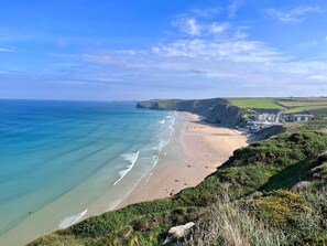A coastal landscape with a sandy beach, cliffs, and a building complex. - 1 Bed in Newquay (oc-o33805) (Newquay)