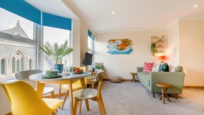 Una sala de estar moderna con comedor, un sofá verde y un televisor en la pared.