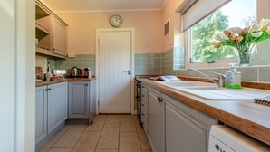 A kitchen with a clock, a window with a view, and a sink with a bottle of hand soap. - 2 Bed in Port Eynon (oc-hh2104) (Port Eynon)