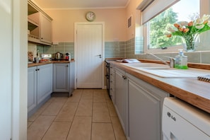A kitchen with a clock, a window with a view, and a sink with a bottle of hand soap. - 2 Bed in Port Eynon (oc-hh2104) (Port Eynon)