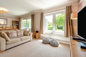 A living room with a sofa, a TV, a bookshelf, and large windows with curtains. - 2 Bed in Port Eynon (oc-hh2104) (Port Eynon)