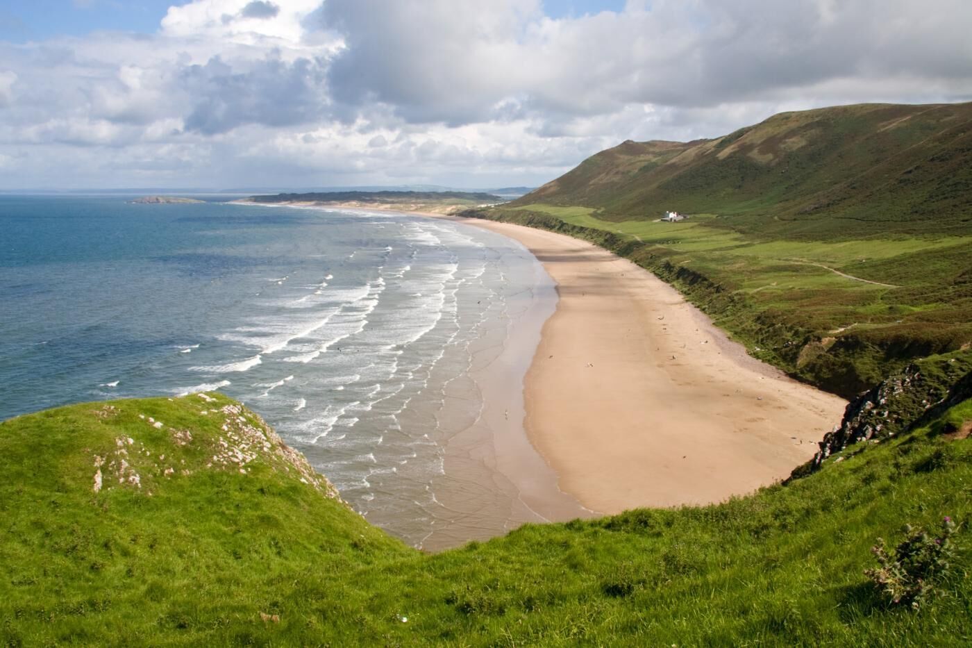 A coastal landscape with a sandy beach, grassy hills, and a clear sky.