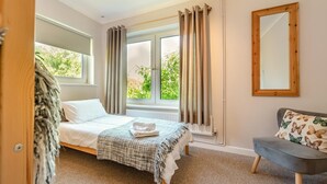 A bedroom with a bed, a grey sofa, a window with curtains, and a mirror on the wall. - 2 Bed in Port Eynon (oc-hh2104) (Port Eynon)
