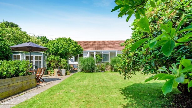 A well-maintained garden with a patio area, a conservatory, and a house with a red-tiled roof. - 2 Bed in Port Eynon (oc-hh2104) (Port Eynon)