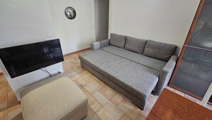 A small, well-lit room with a grey sofa, a small table, and a television. - Three-room In Tortona District (Milano)