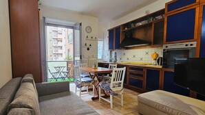 A compact kitchen with wooden cabinets, a dining table with chairs, a sofa, and a television. - Three-room In Tortona District (Milano)
