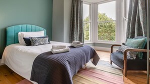 Une chambre à coucher avec un lit, une chaise, une fenêtre et des rideaux.