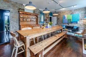 A rustic kitchen with a wooden table, bar stools, and a stone wall. - 7 Bed in Mousehole (oc-boslan) (Paul)