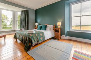 Une chambre à coucher avec un grand lit, deux tables de chevet, une fenêtre avec des rideaux et une vue sur l’extérieur.
