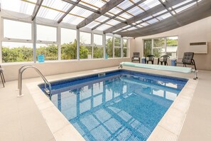 Une piscine intérieure avec des parois en verre transparent, un sol carrelé et un banc le long du bord de la piscine.