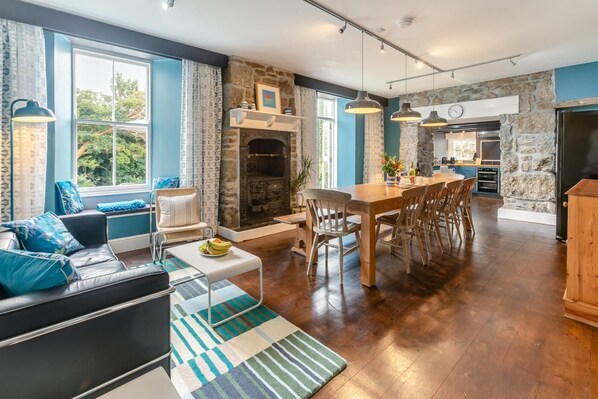 Een ruime woonkamer met een open haard, een eettafel en een keuken met stenen muren.