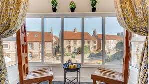 A room with a large window, two wooden chairs, a small table with a tray of items, and three potted plants on the windowsill. - 2 Bed in Sheringham (oc-2264) (Sheringham)