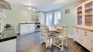 A compact kitchen with a dining area, a washing machine, and a cabinet with glass doors. - 2 Bed in Sheringham (oc-2264) (Sheringham)