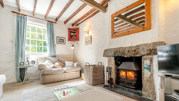 A cozy living room with a stone fireplace, a sofa, a television, and a window with curtains. - 3 Bed in Helford (oc-dowrpe) (Helford)