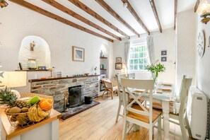 A cozy room with a stone fireplace, wooden beams, a dining table with chairs, and a fruit basket on a wooden table.