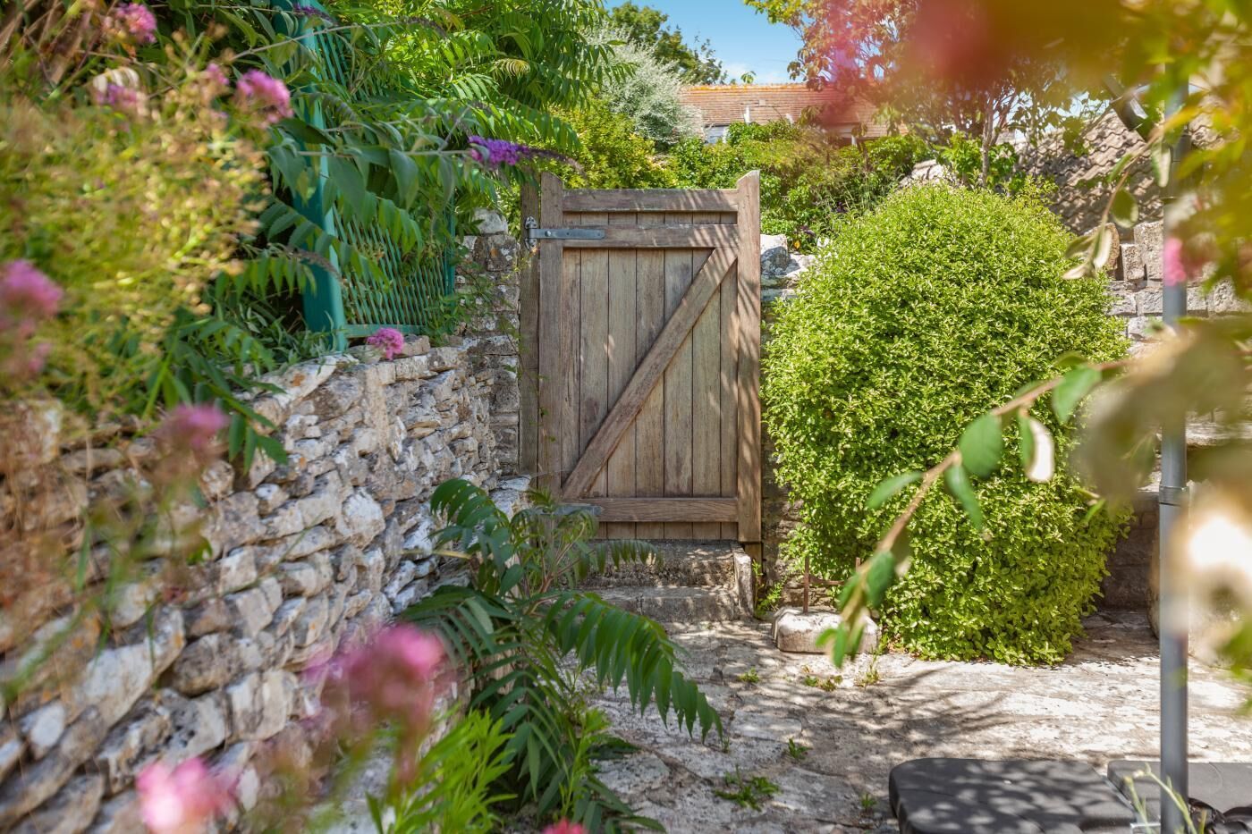 A rustic wooden gate in a garden with stone walls and lush greenery.