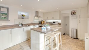 Una cocina moderna con armarios blancos, una isla central con taburetes de bar, un microondas y una campana extractora de acero inoxidable.