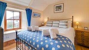 Un dormitorio con cama, mesita de noche, lámpara, reloj, ventana con cortinas e imagen en la pared.