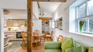 A cozy kitchen with wooden cabinets, a dining area with a wooden table and chairs, and a green sofa by a window with a view of trees. - 3 Bed in Barden (oc-s33752) (Barden)
