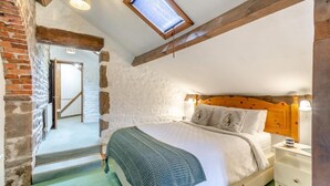 A cozy bedroom with a sloped ceiling, exposed wooden beams, a large window, a bed with a wooden headboard, and a nightstand with a lamp. - 3 Bed in Barden (oc-s33752) (Barden)