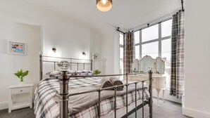 A modern bedroom with a metal bed frame, a bedside table with a lamp, a dresser with a mirror, and a large window with curtains. - 2 Bed in Mumbles (oc-hh59) (The Mumbles)