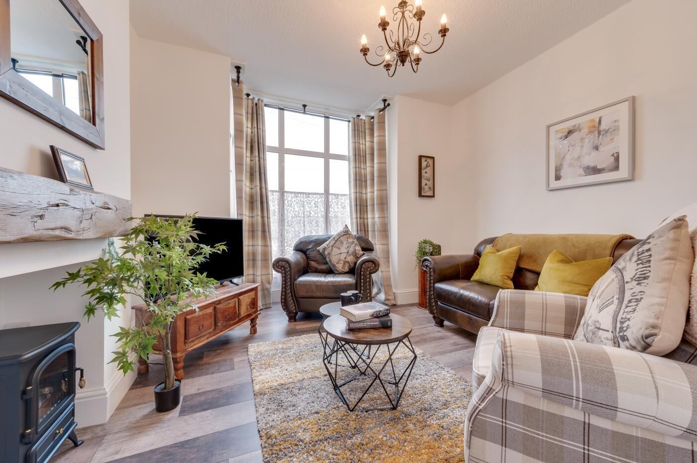 A cozy living room with a fireplace, leather sofas, a coffee table, and a large window with curtains.
