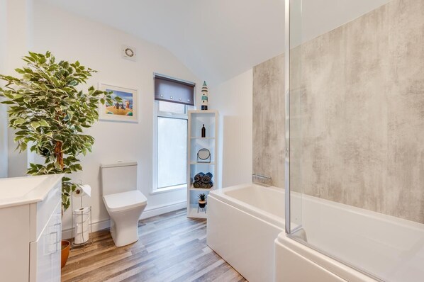 A modern bathroom with a toilet, a shower, and a large potted plant.