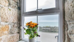 A window with a view of the sea and a stone wall.