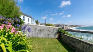A coastal view with a grassy area, a stone wall, and a building with large windows.