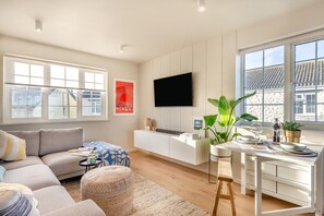 Ein modernes Wohnzimmer mit einer Couch, einem Couchtisch, einem Fernseher und einem Essbereich mit Tisch für zwei Personen.