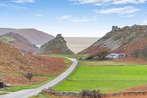 A rural landscape with a winding road, green fields, and rocky hills.