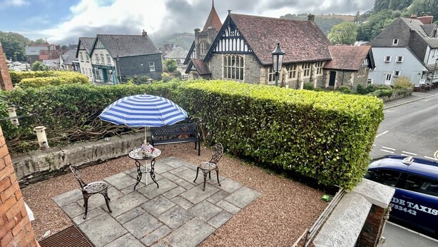 Ein Innenhof mit Tisch, Stühlen, einem gestreiften Sonnenschirm und einer Hecke.