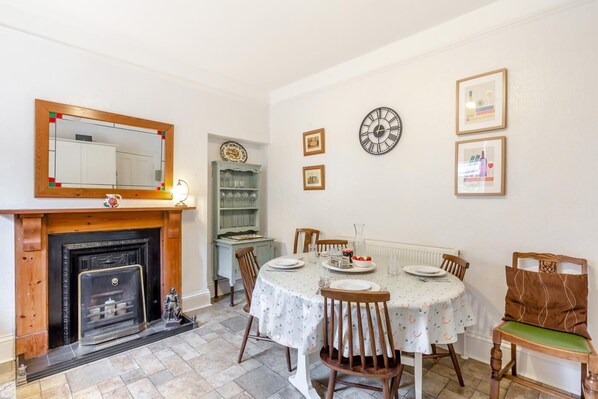 A dining room with a fireplace, a round table set for four, and a mirror above the mantel.