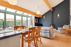 A modern kitchen with wooden chairs, a dining table, and a large window overlooking a garden. - 2 Bed in Holt (oc-2274) (Holt)