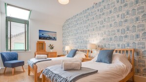 A bedroom with two beds, a chair, a dresser, a painting, and a patterned wallpaper. - 2 Bed in Holt (oc-2274) (Holt)