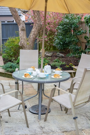 A round glass table with chairs, a yellow umbrella, and a garden setting. - 2 Bed in Holt (oc-2274) (Holt)