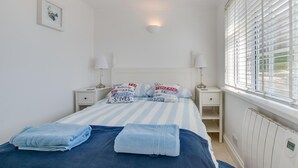 Une chambre à coucher comprenant un lit, deux tables de chevet, une fenêtre avec des stores et un luminaire fixé au mur.