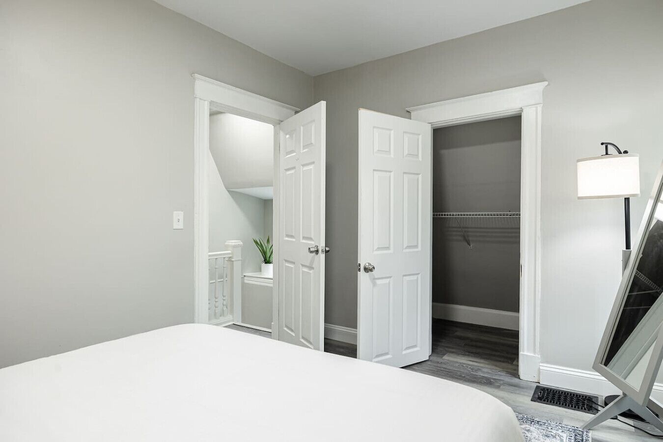 Quarto com uma cama grande, duas portas abertas para um armário e um corredor, e uma luminária de cabeceira.