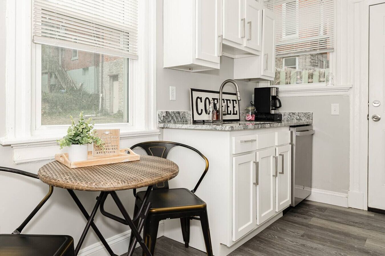 A kitchen with white cabinets, a coffee station, and a wicker table with chairs.