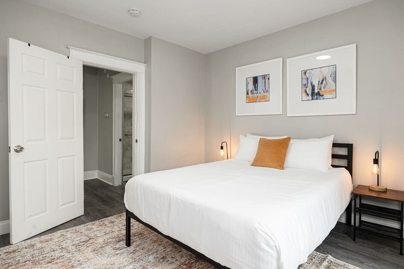Een slaapkamer met een groot bed, een nachtkastje, twee wandlampen en een deur naar een andere kamer.