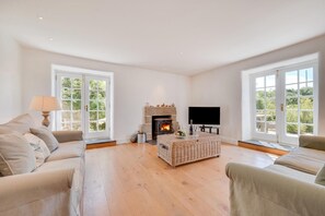 A spacious living room with a fireplace, a television, and large windows. - 3 Bed in Mousehole (oc-kemyel) (Lamorna)